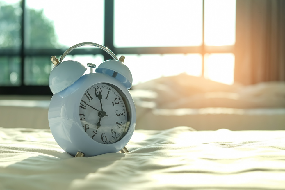 Alarm clock set at 7 o'clock on a white bed.